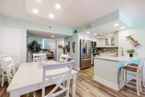 Une cuisine moderne avec des meubles blancs, un îlot central et un coin repas avec des chaises blanches.