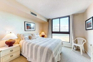 Habitación de hotel con cama, lámparas de noche, una silla y un ventanal con vistas.