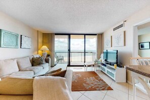Una sala de estar con sofá, televisión, comedor y balcón con vistas.
