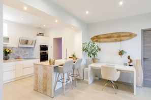 A modern kitchen with white cabinets, a wooden island, and a surfboard decoration. - Villa Cannes 10 min from center - Jacuzzi & Sauna (Le Cannet)