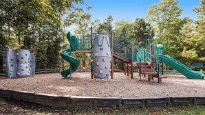 A playground with climbing structures, a slide, and a wooden bench. - Sea Colony 5th Floor Ocean View Condo with Gym (Bethany Beach)