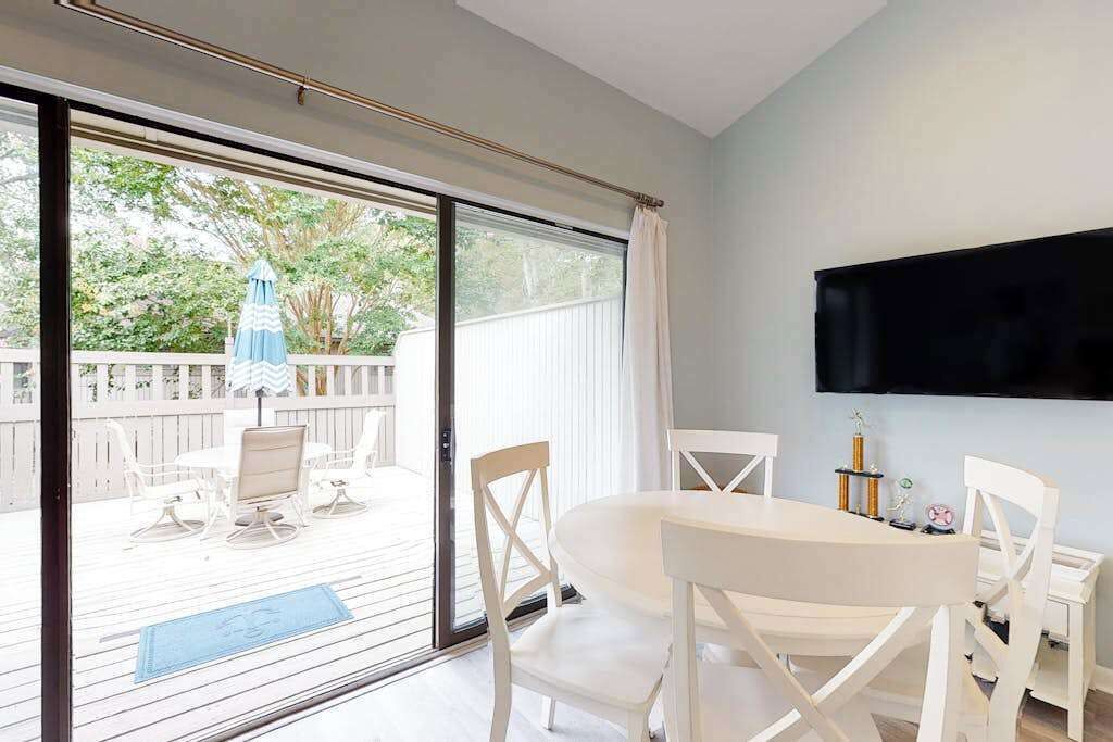 A room with a sliding glass door leading to an outdoor patio, a flat-screen TV mounted on the wall, and a dining table with chairs.