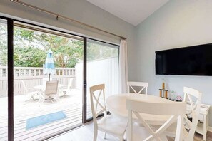 A room with a sliding glass door leading to an outdoor patio, a flat-screen TV mounted on the wall, and a dining table with chairs. - Sea Colony Tennis condo w/ free WiFi, pool, and shared sauna (Bethany Beach)