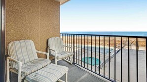 Een balkon met twee gestreepte stoelen, een zwembad en uitzicht op het strand.