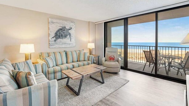Een woonkamer met een bank, een salontafel en uitzicht op het strand door grote ramen.