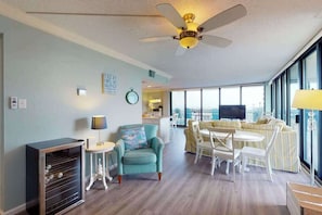 Una sala de estar con ventilador de techo, un sofá, una mesa de comedor con sillas y un televisor.