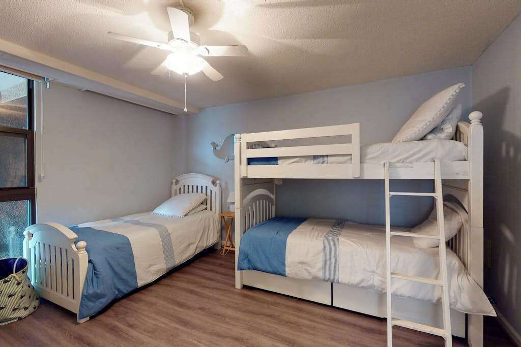 Ein Zimmer mit zwei Etagenbetten, einem Deckenventilator, einem Fenster und einem kleinen Tisch.