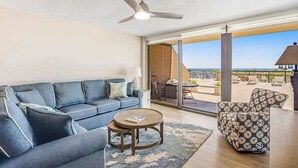 Un salon moderne avec un canapé, une table basse et un fauteuil à motifs, de grandes portes-fenêtres coulissantes donnant sur une terrasse extérieure.