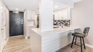 Une cuisine moderne avec des meubles blancs, un îlot central et un tabouret de bar.