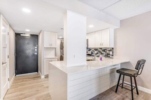 A modern kitchen with white cabinetry, a central island, and a bar stool. - Sea Colony ocean 1st-floor condo with elevator, 12 pools, hot tubs, b-ball court (Bethany Beach)