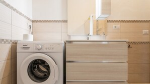Ein moderner Waschraum mit einer Waschmaschine, einem Holzschrank und einer gefliesten Rückwand.