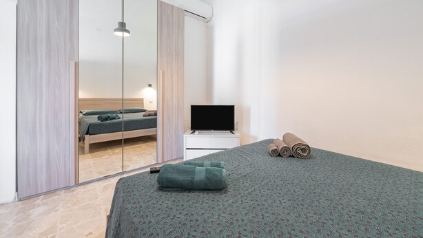 Ein modernes Hotelzimmer mit Bett, Fernseher, Spiegel und Fenster.