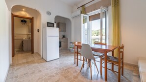 Eine kompakte Küche mit Kühlschrank, Herd und Mikrowelle. Ein Essbereich mit Tisch und Stühlen lädt zum Verweilen ein, und durch ein Fenster bietet sich ein Blick ins Freie.