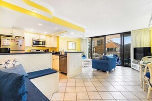 A modern kitchen with a microwave, refrigerator, and dining area with a blue couch and chairs. - Sea Colony Ocean 2nd floor condo with elevator, pool, and gym (Bethany Beach)