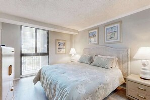 Ein Schlafzimmer mit Bett, Nachttischen, einem Fenster mit Jalousien und Wandbildern.