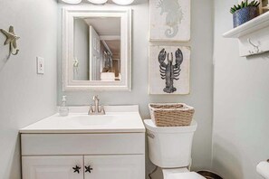 Un baño con tocador blanco, un espejo grande, un inodoro y decoración en la pared.