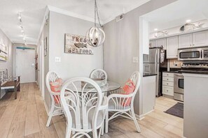 Una cocina moderna con armarios blancos, electrodomésticos de acero inoxidable y un comedor con sillas blancas y una mesa de vidrio.