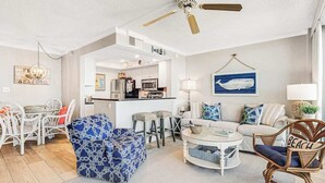 A living room with a sofa, armchair, coffee table, and a dining area with chairs and a table. - Sea Colony Ocean 7th-floor condo with a gym & a tennis court (Bethany Beach)