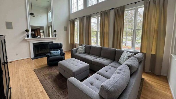 A living room with a sectional sofa, a fireplace, and large windows with curtains. - Bethany Lakes house with a community pool, gym, tennis & free WiFi (Bethany Beach)