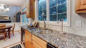 A kitchen with granite countertops, wooden cabinets, a double sink, and a window with a view of trees. - Bethany Lakes house with a community pool, gym, tennis & free WiFi (Bethany Beach)