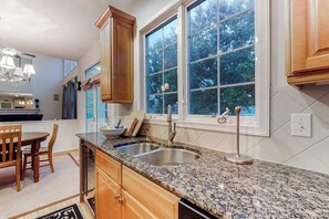 A kitchen with granite countertops, wooden cabinets, a double sink, and a window with a view of trees. - Bethany Lakes house with a community pool, gym, tennis & free WiFi (Bethany Beach)
