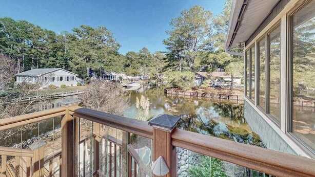 Uitzicht vanaf een balkon over een rivier, met een houten terras, een gebouw met grote ramen en een brug op de achtergrond.
