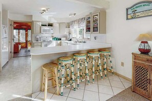 A kitchen with white cabinets, a central island with stools, a microwave, and a sign reading 'Our Beach House'. - South Bethany canal-front house w/ grill, boat dock, and outdoor shower (Bethany Beach)