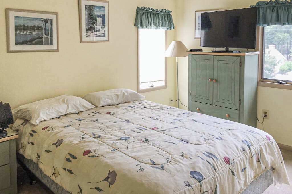 A bedroom with a bed, a television on a cabinet, and framed pictures on the wall.