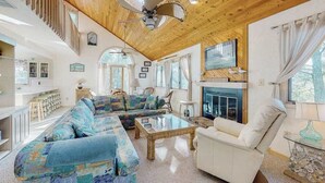 Een ruime woonkamer met een houten plafond, een open haard en een grote bank.