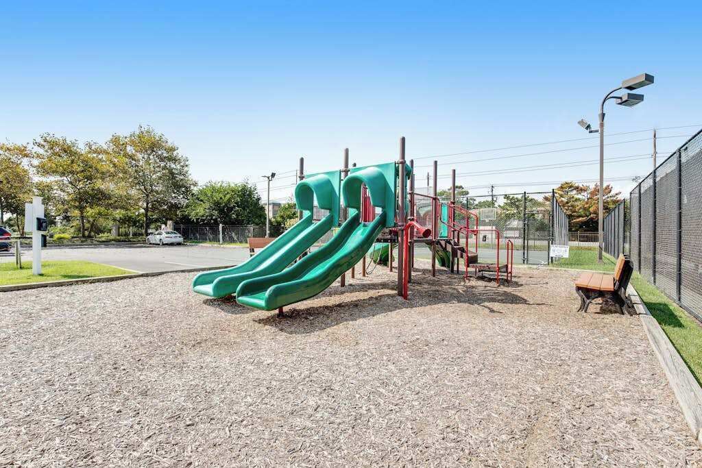 A playground with two green slides, a red climbing structure, and a bench.