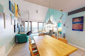 A spacious dining area with a wooden table and chairs, a teal accent wall, and a view through a glass door. - Sea Colony 9th floor condo w/ free WiFi, pool, and balcony with ocean view (Bethany Beach)
