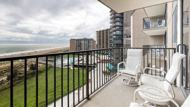 Ein Balkon mit Blick auf den Strand, weißen Stühlen und einem Poolbereich.