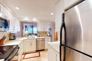 A modern kitchen with stainless steel appliances, white cabinetry, and a red and white rug. - Sea Colony 3rd floor condo w/ ocean view, shared tennis court, elevator, and gym (Bethany Beach)