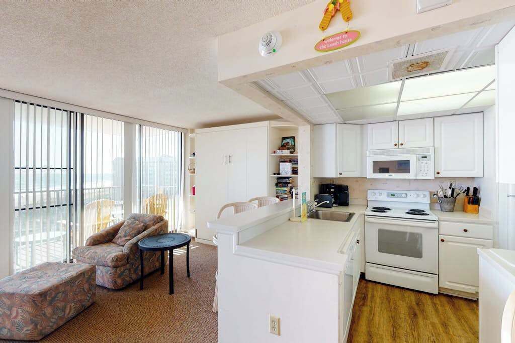 A compact living space with a kitchenette, a sofa, a small table, and a view through large windows.