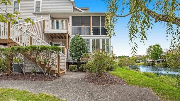 A two-story building with a covered porch, a staircase, and a small garden area. - Sea Colony Tennis 2nd-floor condo with fireplace, basketball court & sauna (Bethany Beach)