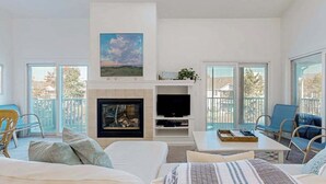 A modern living room with a fireplace, a flat-screen TV, and a balcony with outdoor furniture. - Sea Colony Tennis 2nd-floor condo with fireplace, basketball court & sauna (Bethany Beach)