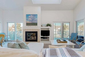 A modern living room with a fireplace, a flat-screen TV, and a balcony with outdoor furniture. - Sea Colony Tennis 2nd-floor condo with fireplace, basketball court & sauna (Bethany Beach)