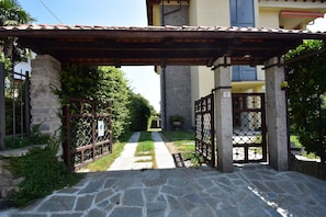 Ein gepflasterter Weg führt zu einem Eingangstor mit einer Pergola darüber.