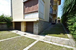 Ein Wohngebäude mit einer Stein-Fassade, einer braunen Markise über dem Eingang und einem kleinen Garten mit einem Steinweg.