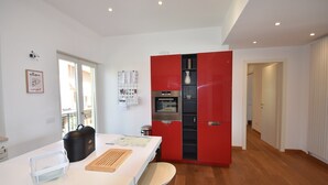 Uma cozinha moderna com bancada branca, armário vermelho e chão de madeira.