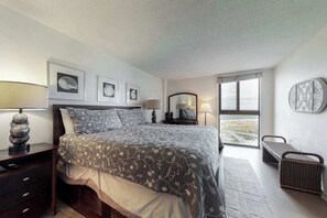 A bedroom with a bed, bedside tables, lamps, framed pictures, a window, and a view. - Sea Colony 7th floor condo w/ shared basketball court, balcony & ocean view (Bethany Beach)