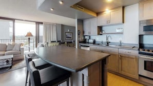Uma cozinha moderna com ilha central, eletrodomésticos embutidos e sala de jantar com sofá e cadeiras.