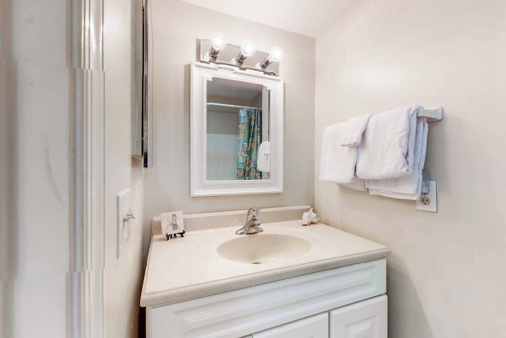A bathroom with a white sink, a mirror with lights, and a towel rack.
