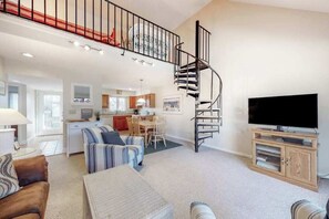 A spacious living area with a spiral staircase, a flat-screen TV, and a dining area. - Sea Colony Tennis 2nd-floor condo with pool access (Bethany Beach)