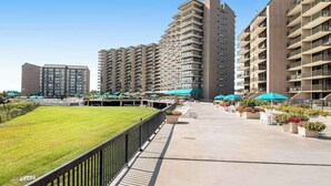 Un moderno complejo de apartamentos con varios edificios de gran altura, un patio central con asientos y vegetación, y un cielo despejado.