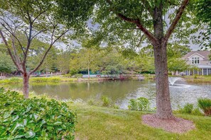 A tranquil park with a pond, trees, and a building in the background. - Sea Colony Tennis townhouse with tennis court, sauna, & pool (Bethany Beach)
