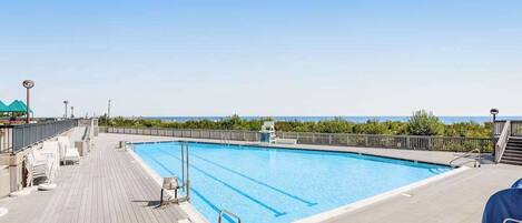 A swimming pool with clear blue water, surrounded by a wooden deck, and a view of the ocean.