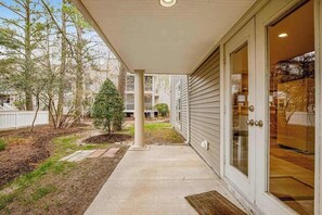 A covered patio with a concrete path, a small tree, and a white fence. - Sea Colony Tennis townhouse with gym, pool, tennis court, & basketball court (Bethany Beach)