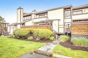 A modern two-story house with a covered patio, a small garden, and a wooden fence. - Sea Colony Tennis townhouse with basketball court, pool & sauna (Bethany Beach)