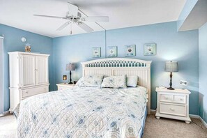 Een slaapkamer met een bed, een plafondventilator, een nachtkastje, een lamp en een kledingkast.